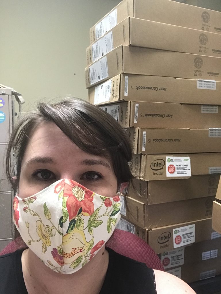 Meredith wearing a mask in front of boxes of laptops.