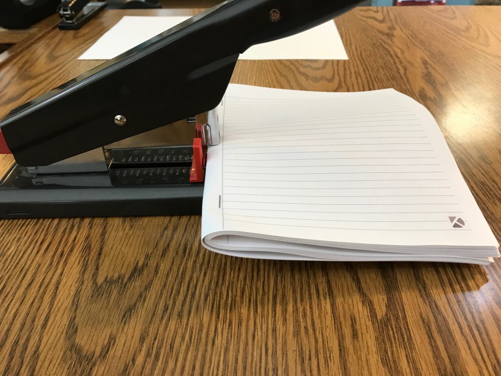 A large stapler stapling the middle of the folded interior pages