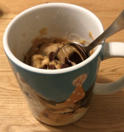 A chocolate chip peanut butter cookie mug cake with a spoon sticking out-- the mug has angry cats wearing party hats