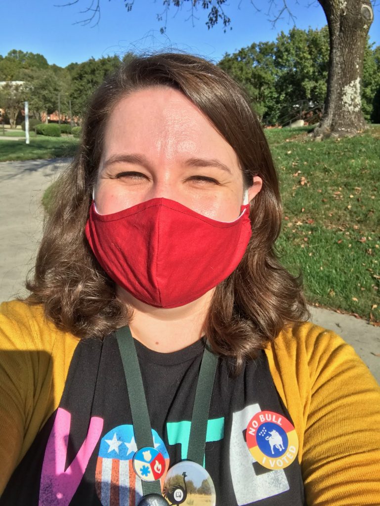 Meredith squinting in the sun with a red mask, a Vote Now t-shirt, and a No Bull-- I Voted sticker