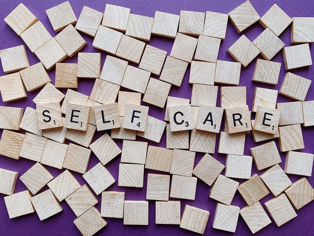 A set of Scrabble tiles, some turned over so they are blank in the background, with the words SELF CARE spelled out on top