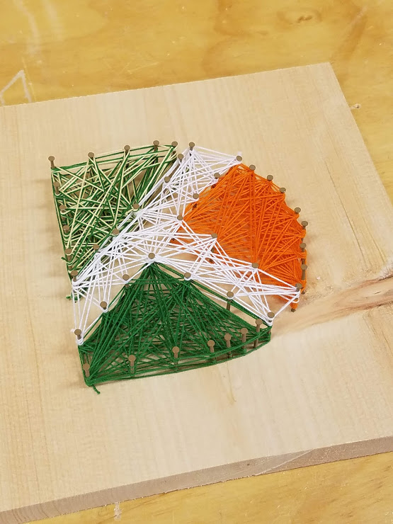 Durham Tech D logo in greens, orange, and white made of string and nails on blonde wood